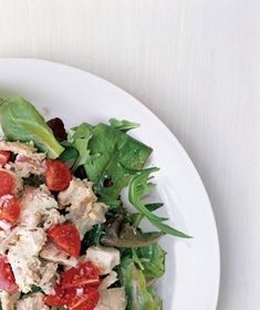 a white plate topped with salad covered in meat and veggies on top of it