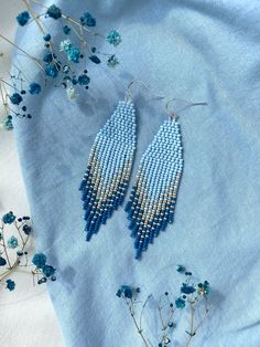 two pairs of beaded earrings sitting on top of a blue cloth next to flowers