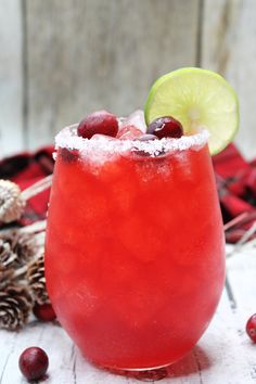 a red drink with cranberries, lime and sugar on the rim next to pine cones