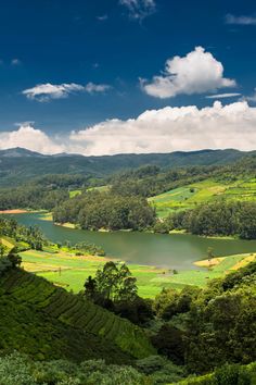 a lake surrounded by lush green hills under a blue sky with white clouds in the distance