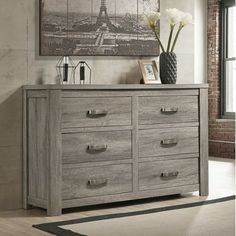 a dresser with drawers in front of a painting on the wall and flowers sitting on top of it