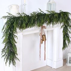 a white fireplace decorated with greenery and bells