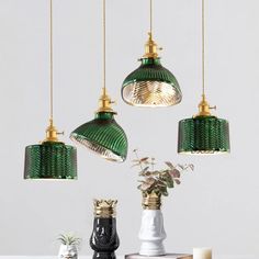 three green and gold pendant lights hanging from the ceiling above a table with two vases on it