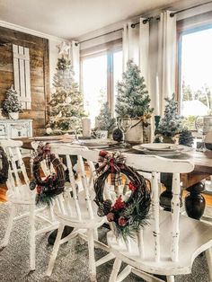 a dining room table with wreaths on it and christmas decorations around the table in front of large windows