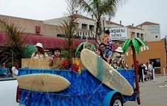 people riding in the back of a blue truck with surfboards on it's flat bed