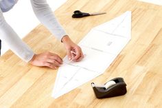 a person cutting out a paper airplane on top of a wooden table next to scissors