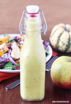 a salad dressing in a glass bottle next to an apple and other food on a table