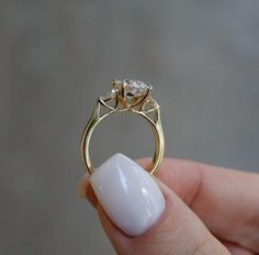 a hand holding a gold ring with two diamonds on it's sides and a white nail