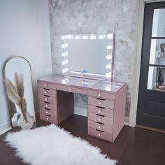 a pink vanity with lights on it and a white sheepskin rug in front of the mirror