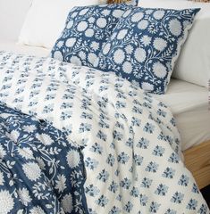 a bed with blue and white comforter on it's side, next to a night stand