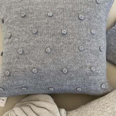 a gray pillow with holes on it next to a white blanket and a ball of yarn