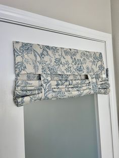 a blue and white window valance hanging on the side of a door in front of a mirror