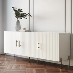 a white sideboard with two brass handles and a potted plant sitting on top