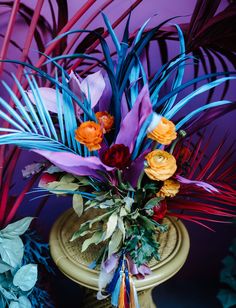 a vase filled with colorful flowers on top of a table next to green plants and purple walls