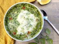 a bowl filled with spinach and cheese next to a slice of lemon on top of a yellow towel