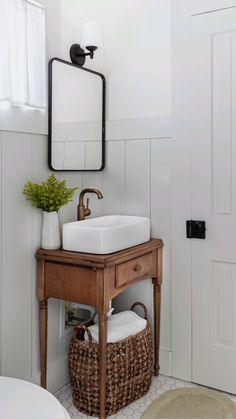 a bathroom sink with a mirror above it and a basket under the sink next to it