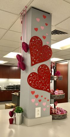 two red hearts are hanging on the side of a tall pillar in an office cubicle