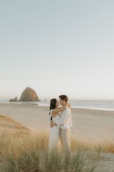 an engaged couple embracing on the beach in front of some tall grass and sand dunes