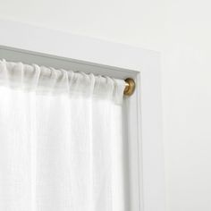 a white curtain with gold hardware hanging on the side of a window in a room