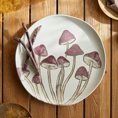 a plate with purple mushrooms painted on it sitting on a wooden table next to other plates and utensils