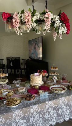 a table topped with lots of cakes and desserts under a chandelier filled with flowers