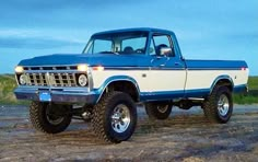 a blue and white truck parked on top of a dirt field