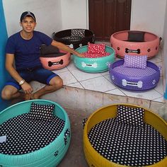 a man sitting on the ground in front of several large, colorful dog beds with polka dots