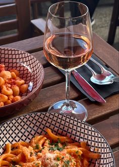 two bowls of pasta and a glass of wine on a table