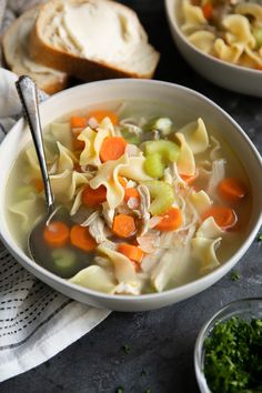 two bowls filled with pasta and carrots next to some bread on a cloth napkin