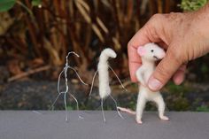 a hand holding a tiny toy mouse in front of two smaller ones on a table