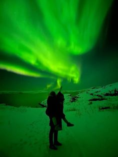 two people are standing in the snow under an auroral sky filled with green lights