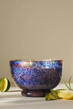 a blue bowl sitting on top of a table next to sliced lemons and a candle