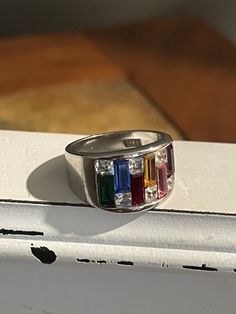 This is a stunning 1980s mixed colorful gemstone fashion ring. The faceted baguette cut gemstones are vibrant, bright and clear. Staggered in between are 6 square clear crystal gems.   ] Gemstones include: Deep green Emerald, Deep Blue Sapphire, Red Garnet, Citrine, Pink Tourmaline, Purple Amethyst  Size 9-9.5 18k  GE White Gold/silver   Inside is etched: 18K followed by 2 letters that appear to be GE. Multicolor Gemstone Rings With Baguette Cut, Multicolor Baguette Cut Gemstone Rings, Multicolor Gemstone Baguette Cut Rings, Multicolor Gemstone Sapphire Ring In Sterling Silver, Multicolor Multi-stone Emerald Cut Rings, Multicolor Emerald Cut Multi-stone Rings, Multicolor Multi-stone Baguette Cut Rings, Multi-stone Enamel Ring Jewelry, Black Statement Ring