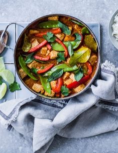 a pan filled with chicken, peppers and rice next to a bowl of limes