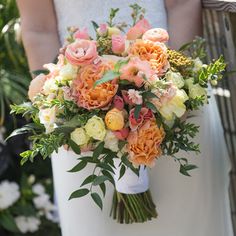 a bridal holding a bouquet of peach and white flowers with greenery in the background