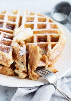 a white plate topped with waffles covered in powdered sugar next to a fork