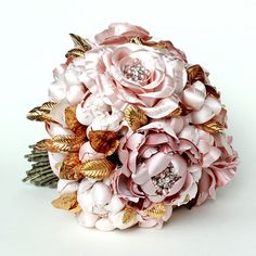 a bridal bouquet with pink flowers and gold leaves on the bottom, sitting on a white surface