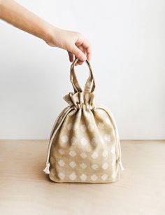 a hand is holding onto a polka dot bag on a wooden table with a white wall in the background