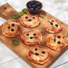 small pizzas with black olives and cheese are arranged on a wooden cutting board