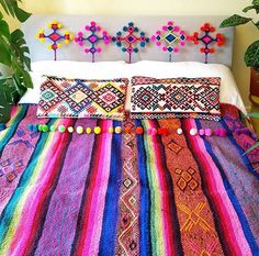 a bed covered in multi colored blankets and pillows with pom poms on the headboard