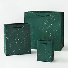 three green bags sitting next to each other on top of a white surface with gold speckles