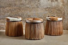 three wooden stools with hair on them in front of a stone wall and cement floor