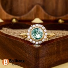 a close up of a ring in a wooden box with pearls and a green stone