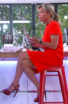 a woman in a red dress is sitting on a stool and looking at her tablet