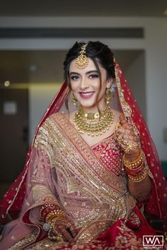 a woman in a red and gold bridal outfit posing for the camera with her hands on