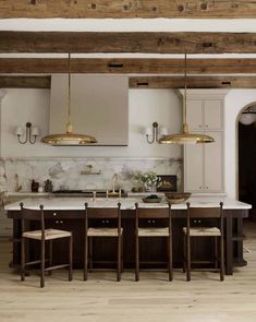 a large kitchen with marble counter tops and wooden chairs in front of an island that has gold pendant lights hanging from the ceiling