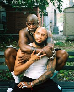 two men sitting on a bench hugging each other with one holding the other's arm