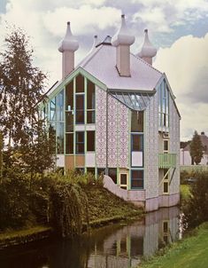 an unusual house sits next to a body of water in the middle of a grassy area