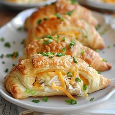 three croissants on a white plate topped with cheese and green onions next to other pastries