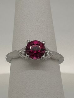 This natural round Rhodolite Garnet is 1.45ct purplish red and set in a 14K white gold ring size 7 (sizable) with .02ctw VS G-H Diamond Melee.  Each side of the ring as a heart-shape with a 1.4mm diamond set inside.  The name Rhodolite is derived from the Greek "rhodon" for "rose-like".  This stone has great color, cut and clarity. Garnet is the birthstone for the month of January. I am a GIA Graduate Gemologist with a passion for all gemstones.  I have a 30 day return policy so if do not wish to keep this item, simply return to me for your refund. Clarity        Eye-Clean Carat Weight1.45 carats Shape         Round Cut                Step Cut Enhancement (N) None  Gemstone Enhancement Codes*  N = Not Enhanced B = Bleaching C = Coating  D = Dyeing F = Filling H = Heating  HP = Heat & Press 14k White Gold Ruby Ring With Brilliant Cut, Red Round Solitaire Sapphire Ring, Ruby Ring With Brilliant Round Cut, Red Solitaire Sapphire Ring, Garnet Rings With Accent Stones, Classic White Gold Ruby Ring With Round Stone, Round Garnet Diamond Ring With Prong Setting, Lab-created Ruby Diamond Ring With Prong Setting, Fine Jewelry Round Ruby Solitaire Ring